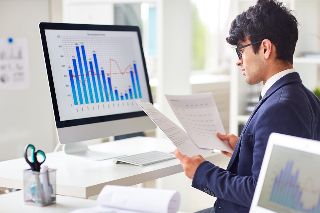 Businessman looking through papers by workplace and analyzing statistics